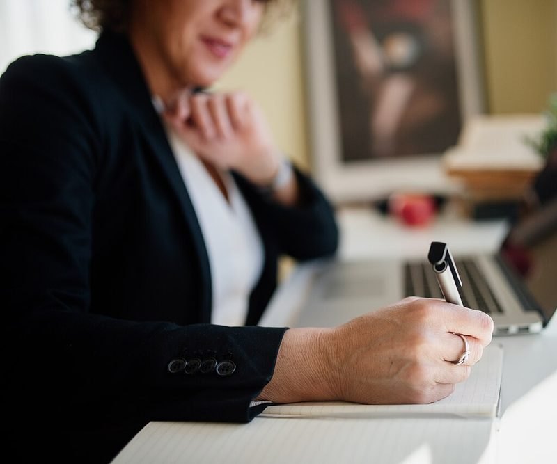 A professional taking notes beside a laptop during a review meeting